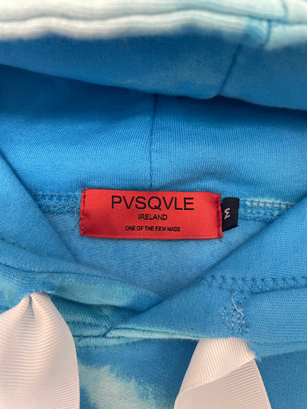 Close-up of a blue fabric with a red label featuring 'PVSQVLE' branding.