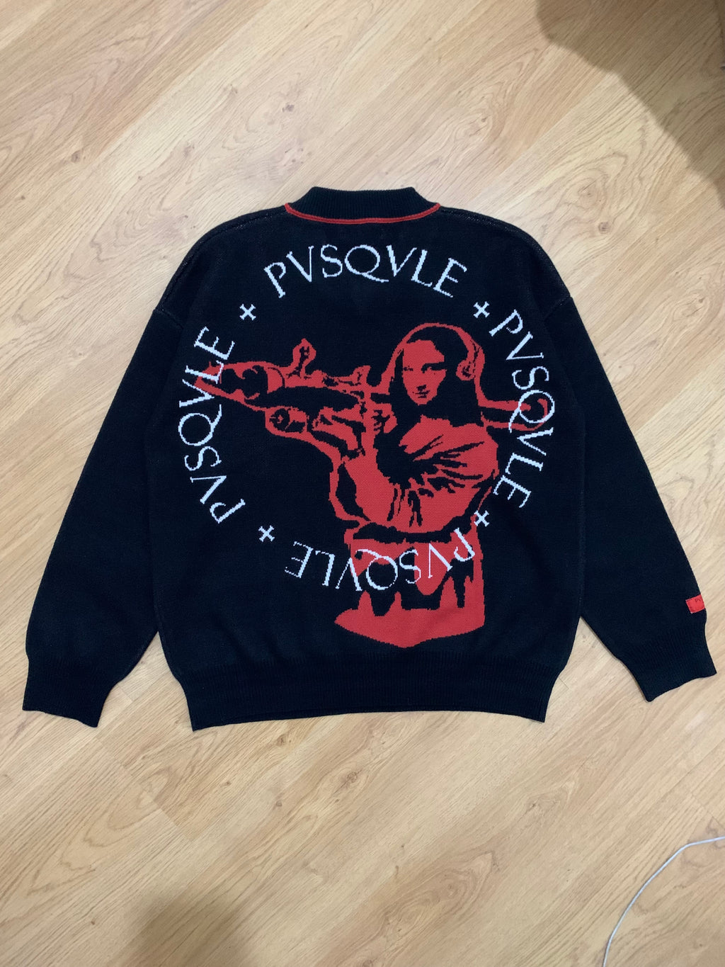 Black sweater with red and white monalisa graphic design on a wooden floor